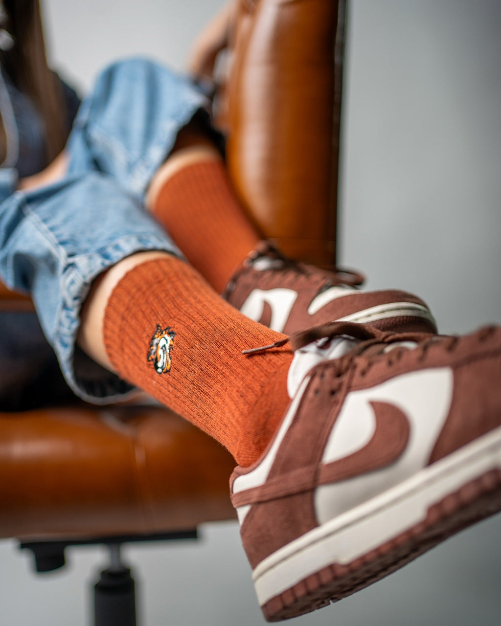 Archive Set für Damen von Good Willy: Orange Crew-Socken zu braun-weißen Sneakern auf einem Ledersessel (KI-generiert)