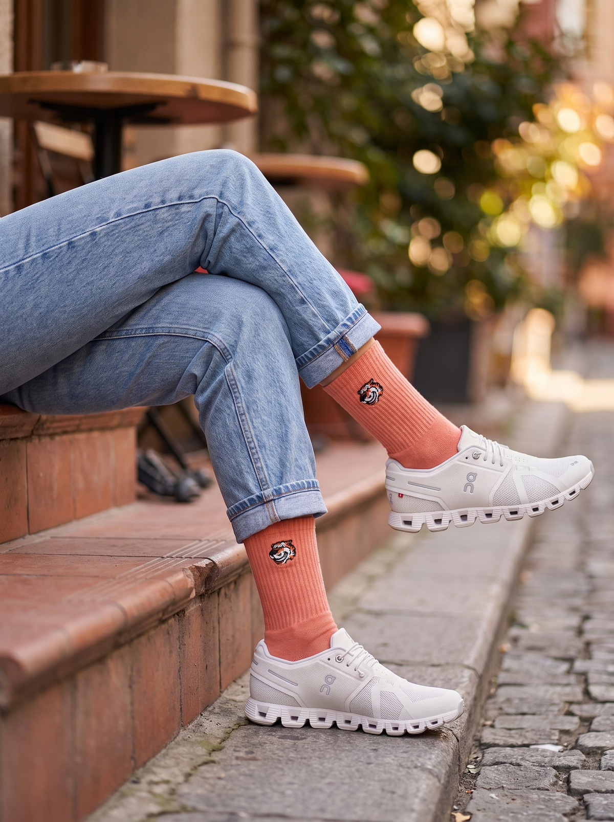 Frau sitzt auf Stufen und trägt Bellini Breakfast Crew-Socken in Pfirsich von Good Willy zu weißen Sneakern (KI-generiert)