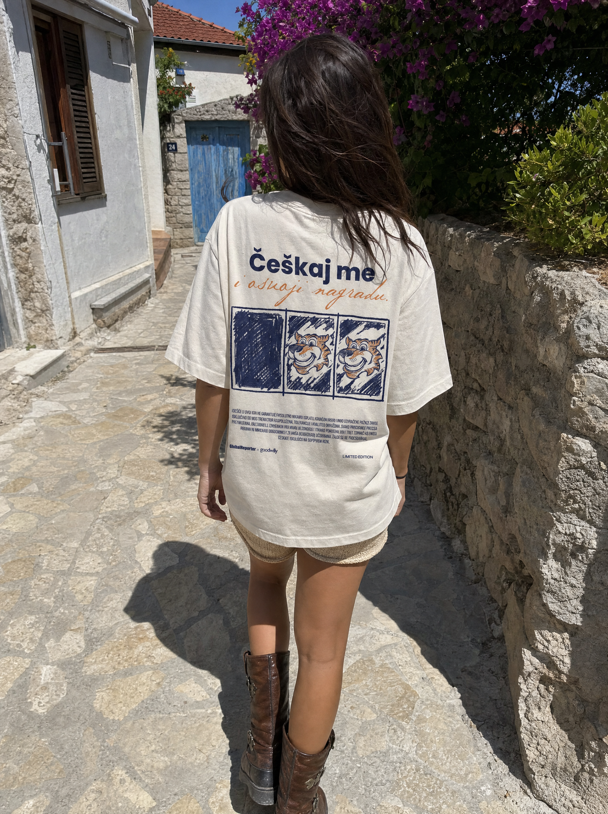 Češkaj me T-Shirt von Good Willy, getragen von einer Frau in einer Altstadtgasse, Rückansicht (KI-generiert)