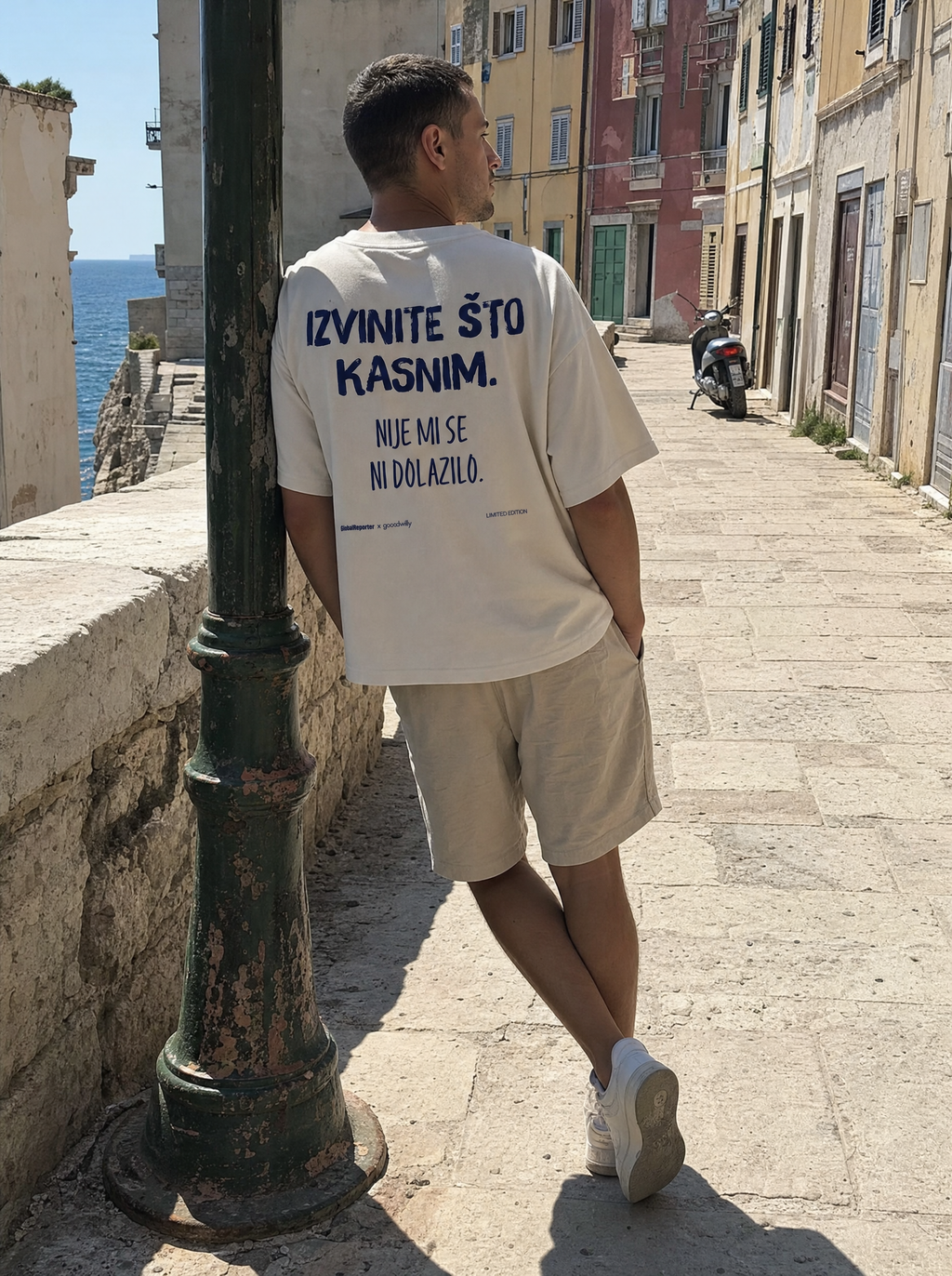 Izvinite što kasnim T-Shirt von Good Willy, getragen von einem Mann in einer Altstadtgasse, Rückansicht (KI-generiert)